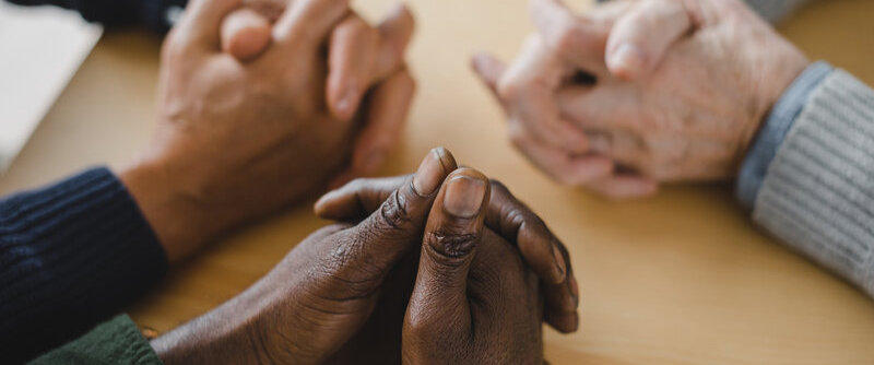 Group of multiethnic people at a table with open bibles, praying